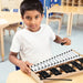 Young boy playing a 27-note glockenspiel xylophone with black and white metal bars in a classroom
