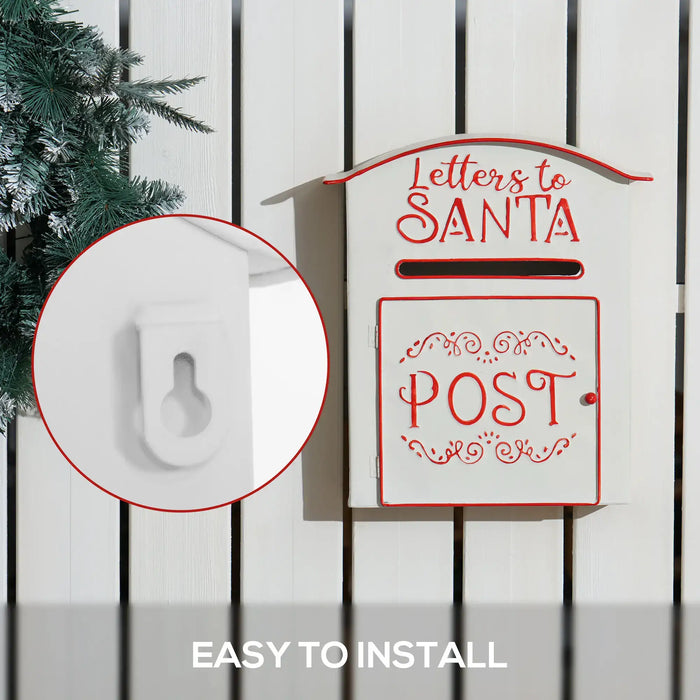 White and red metal mailbox labeled Letters to Santa Post mounted on white wooden fence with evergreen branches