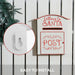 White and red metal mailbox labeled Letters to Santa Post mounted on white wooden fence with evergreen branches