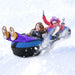 Two kids laughing and sledding on a blue and black inflatable snow tube in deep snow