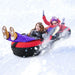 Two kids in winter clothes sliding down snowy hill on red and black inflatable snow tube