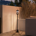Black outdoor garden lamp post illuminating patio next to beige wall and dried ornamental grass at dusk