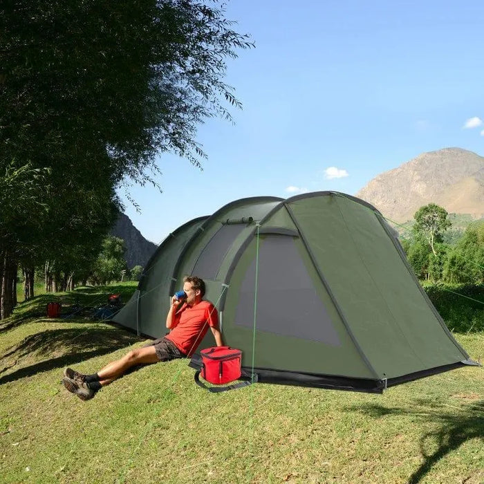 Green 3-4 person dome tent with two rooms set up outdoors, camper relaxing beside it