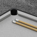 Compact grey pool table corner with two wooden cues on carpeted floor
