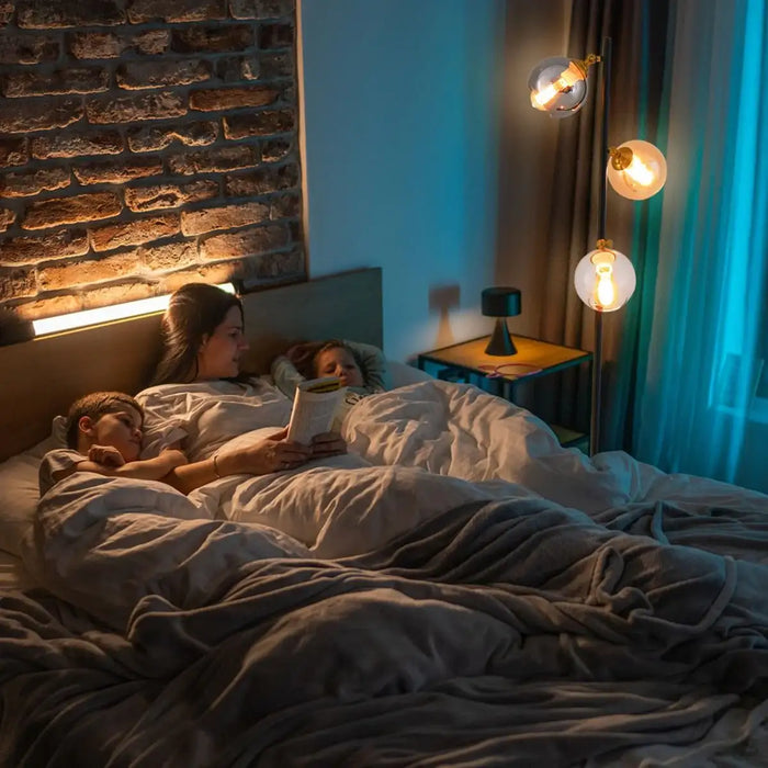 Woman reading a book to a child in bed with soft lighting.