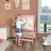 Child drawing on pink kids easel with animal storage bins in playroom by window