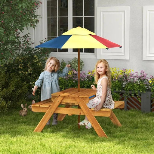 Kids sitting at wooden picnic table with colorful umbrella in garden setting