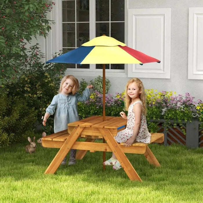 Kids sitting at wooden picnic table with colorful umbrella in garden setting