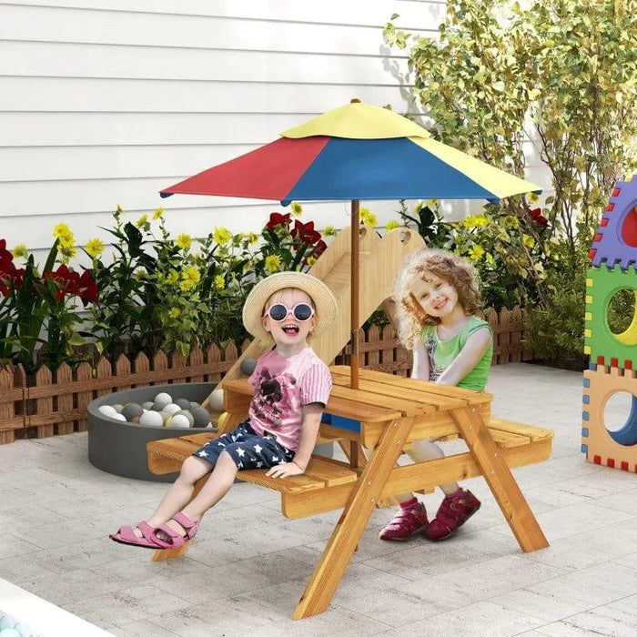 Kids sitting at wooden picnic table with colorful umbrella in backyard play area
