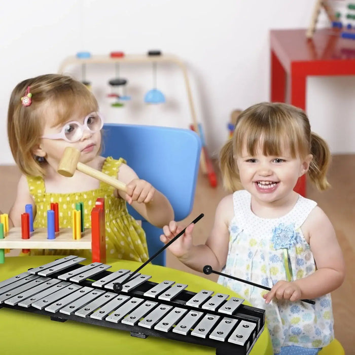 Two young girls playing musical toys indoors, one with wooden mallet and other with xylophone mallets
