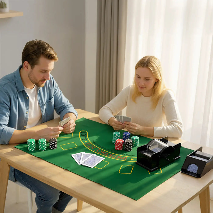 Man and woman playing cards at table with green casino mat, poker chips, card shuffler, and shoe