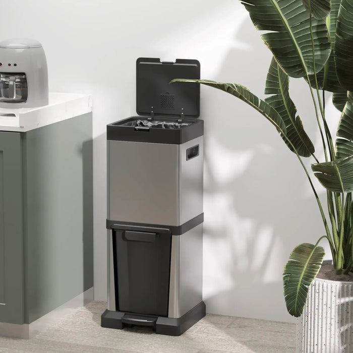 Stainless steel trash can with black lid and base in a room with a plant and kitchen appliance.