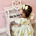 Young girl in floral dress with bow playing white kids piano with microphone in pink room