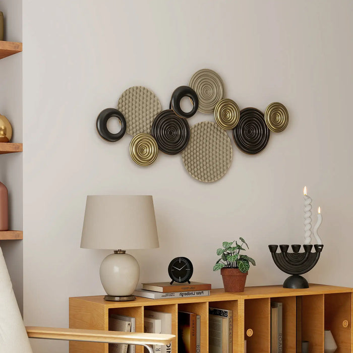 Decorative wall art with circular patterns on a wall above a wooden shelf with books and a lamp.