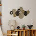 Decorative wall art with circular patterns on a wall above a wooden shelf with books and a lamp.