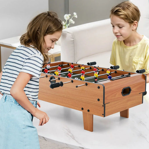 Two children playing with a foosball table in a living room.