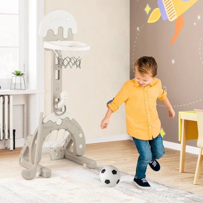 Child in yellow shirt playing with a grey 4-in-1 kids activity center featuring basketball hoop and soccer goal indoors