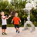 Two boys playing basketball outdoors near a grey 4-in-1 kids activity center with dual basketball hoops