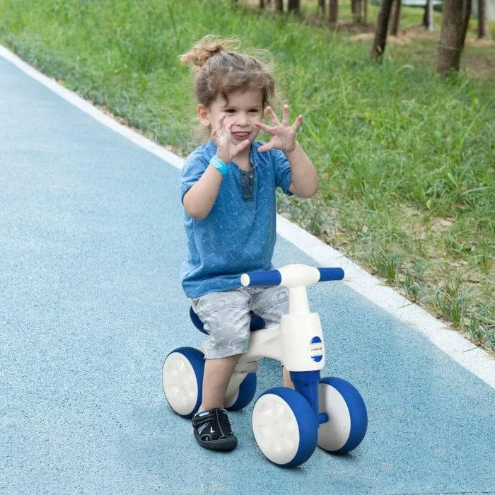 Child riding white and blue 4-wheel kids’ balance bike on outdoor path