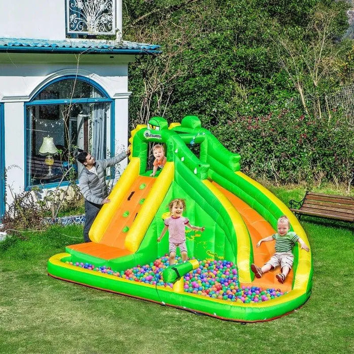Kids playing on green and orange inflatable bounce house with slide, ball pit and climbing wall in garden