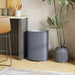 Gray trash can next to a plant in a room with a table and chairs.