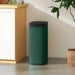 Modern green touchless sensor trash bin with black lid in minimalistic kitchen corner