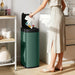 Woman in light dress using green automatic touchless sensor kitchen trash bin with black lid