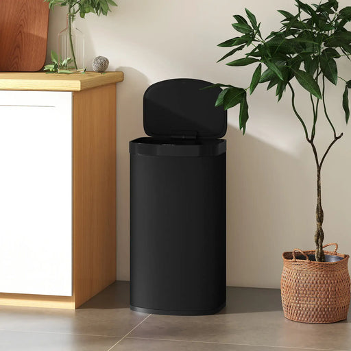 Black trash bin next to a potted plant in a room with wooden furniture.