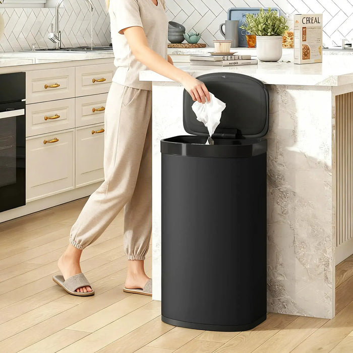 Person disposing of trash into a black trash can in a kitchen.