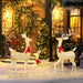 Glowing light-up Christmas reindeer family with red bows in snow outside festive decorated stone house