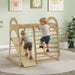 Two children playing on a wooden climbing toy in a room with light green walls and decorative elements.