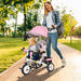 Woman pushing a child in a pink stroller along a path in a park.