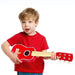 Young child in red shirt playing a red 6-string kids acoustic guitar on white background