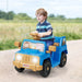 Young boy riding a blue and tan kids' toy car on a gravel path with cartoon animal decals