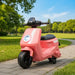 Pink toy scooter with black wheels in a park setting
