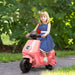 Young girl riding a pink toy scooter outdoors with greenery in the background