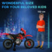 Red kids electric motorcycle with training wheels next to a 132 cm tall boy in orange shirt and denim shorts