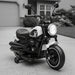 Black and white kids electric motorcycle with training wheels parked on driveway in front of house
