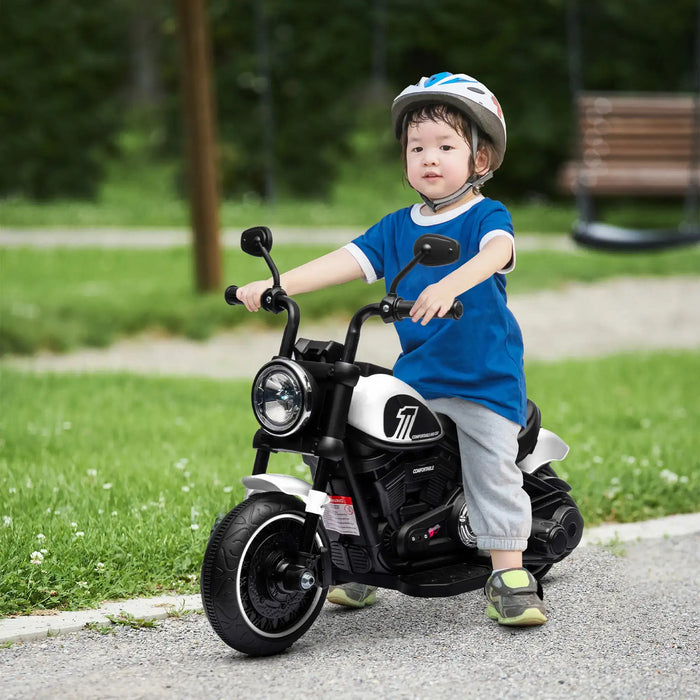 Toddler wearing helmet riding black and white electric toy motorcycle outdoors on paved path