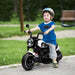 Toddler wearing helmet riding black and white electric toy motorcycle outdoors on paved path