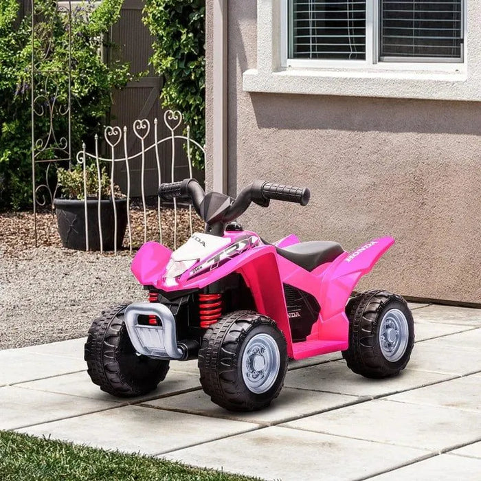 Pink kids Honda ride-on quad bike with LED lights parked on patio near house window