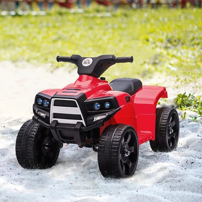 Red kids ride on quad ATV bike with black wheels parked outdoors on sandy ground