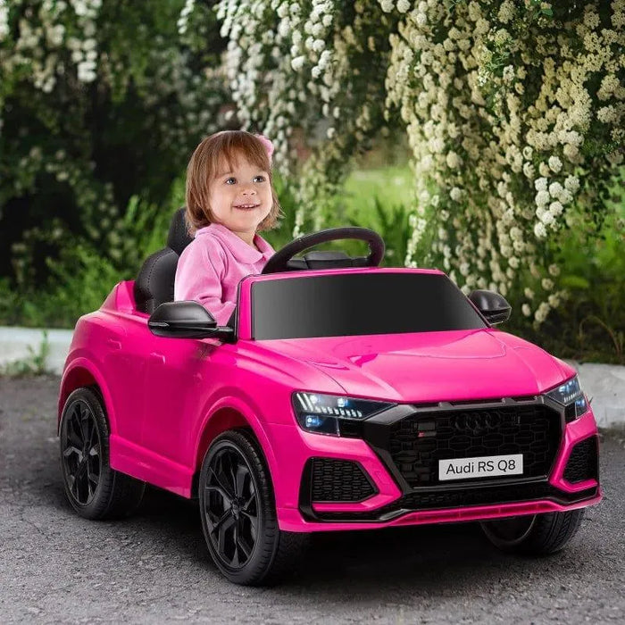 Child driving pink Audi RS Q8 kids electric ride-on car outdoors with flowers in background