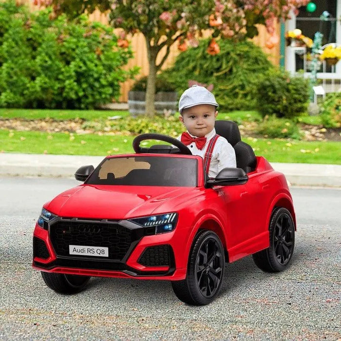 Child in red Audi RS Q8 kids ride-on car outdoors, wearing a cap and suspenders.