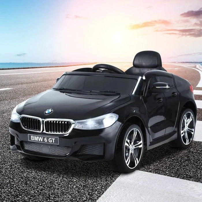 Black BMW 6 GT kids ride-on car toy on outdoor road at sunset