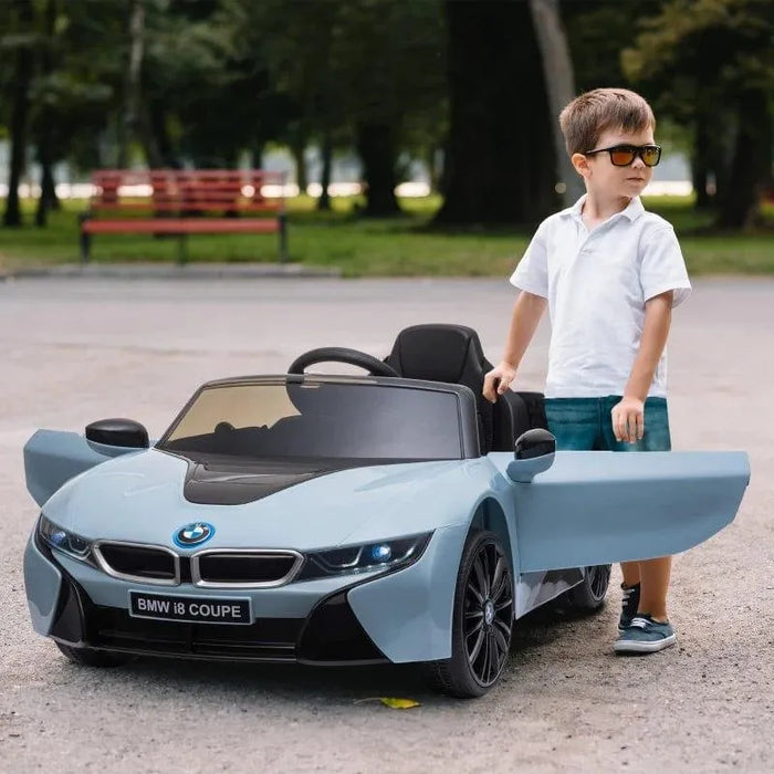 Boy in sunglasses stands next to blue BMW i8 coupe kids electric ride-on car with open doors