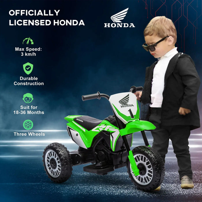 Toddler in sunglasses stands by green Honda kids' electric ride-on motorbike with three wheels.
