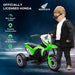 Toddler in sunglasses stands by green Honda kids' electric ride-on motorbike with three wheels.