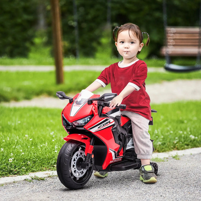 Toddler riding red Honda kids' electric motorbike outdoors on paved path.