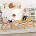 Two children playing on a colorful wooden climbing toy in a room with books and decor.